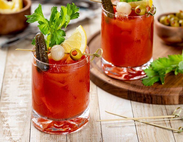 Bloody mary cocktail garnished with celery, lemon, pickle, onion and olive on a wooden table - Foto, Imagen