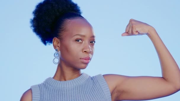 Erős, izom és arc egy fekete nő bicepszekkel elszigetelt kék háttér egy stúdióban. Komoly, magabiztos és portré egy afrikai lány a hatalom, felhatalmazás és mutatja tornaterem fejlődését. - Felvétel, videó