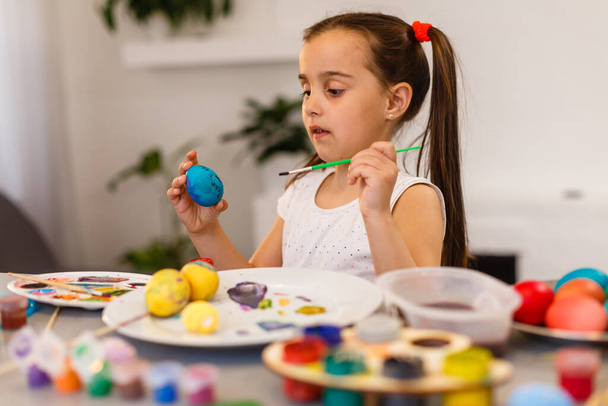 Милая маленькая девочка рисует яйца кисточкой. Пасхальная концепция - Фото, изображение