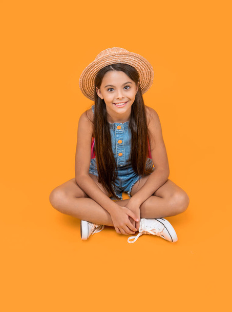 happy teen girl in straw hat sitting on yellow background. - Foto, Imagen