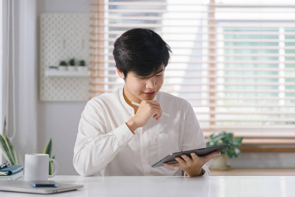 A smiling young millennial businessman is holding and using a digital tablet computer with online apps and software on a modern tech device. - Photo, Image