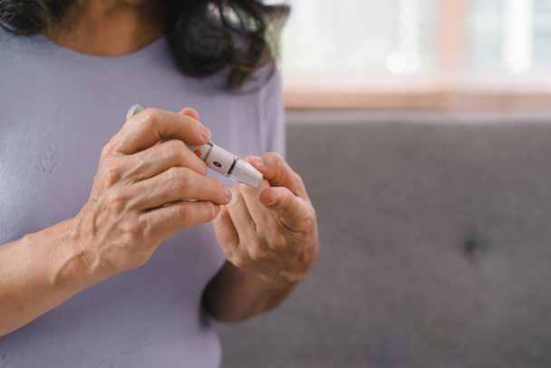 Gros plan de la main d'une aînée qui vérifie son taux de sucre dans le sang avec un glucomètre toute seule chez elle - Photo, image