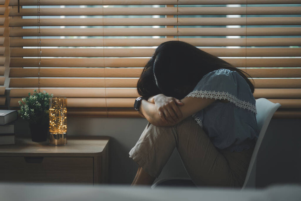 Smutna i przygnębiona młoda kobieta siedząca nere okno w salonie, spoglądająca na zewnątrz ze smutnym wyrazem twarzy, przekazująca uczucia wyczerpania, samotności i nieszczęścia - Zdjęcie, obraz