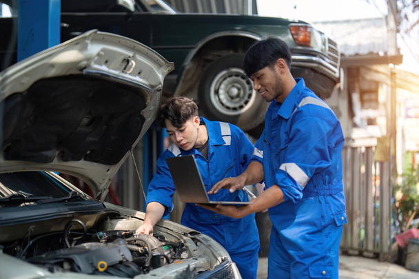 Mechanik pokazuje raport azjatyckiemu współpracownikowi w garażu, mechanikowi i jego synowi omawiającemu naprawę pojazdu. Zmiana branży motoryzacyjnej.. - Zdjęcie, obraz