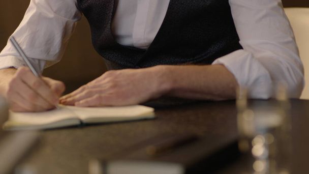 Egy közeli kép ismeretlen fiatal író férfi kezeiről és jegyzetfüzetéről. Az író jegyzetel egy jegyzetfüzetben. - Fotó, kép