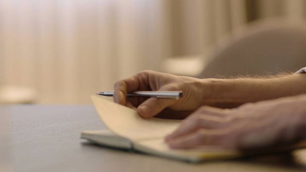 Close-up of male hands and notebook of unidentified young writer. The writer makes notes in a notebook - Foto, imagen