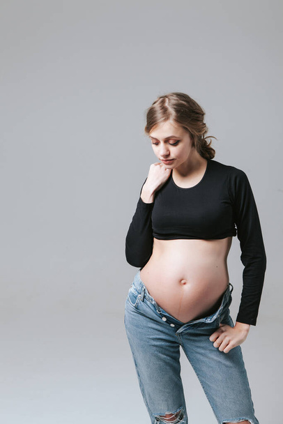 Young pregnant girl in jeans on a white background - Fotografie, Obrázek