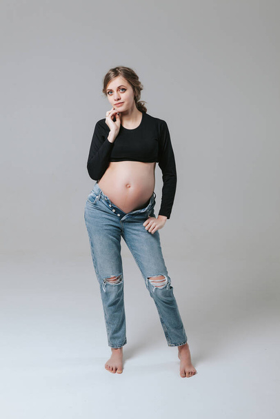 Young pregnant girl in jeans on a white background - Фото, зображення