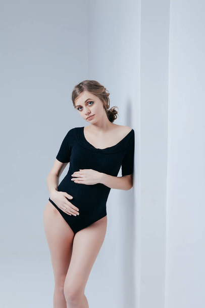 Молода вагітна дівчина в чорному боді на білому тлі
 - Фото, зображення