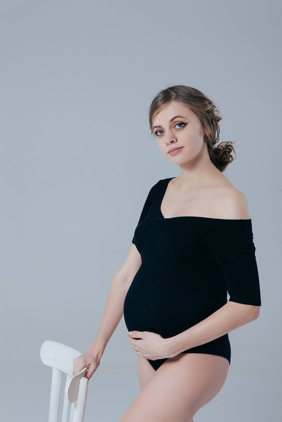A young pregnant girl in a black bodysuit on a white background - Fotó, kép