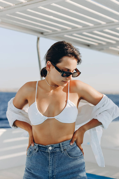 Denizdeki bir teknede seksi bir kız. Kız tatilde. Güneş gözlükleriyle el ele tutuşun. Beyaz bir mayoyla - Fotoğraf, Görsel