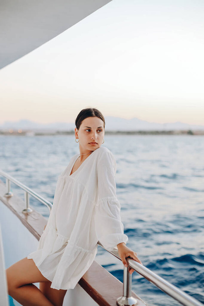 青い海を背景に、ボートのデッキの近くに立って、白い繊細なドレスの少女の肖像画。 - 写真・画像
