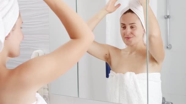 Mujer sonriente en toalla de baño levantando los brazos y mostrando el pelo largo y oscuro de la axila. Concepto de higiene, belleza natural, feminidad y crecimiento del vello corporal - Imágenes, Vídeo