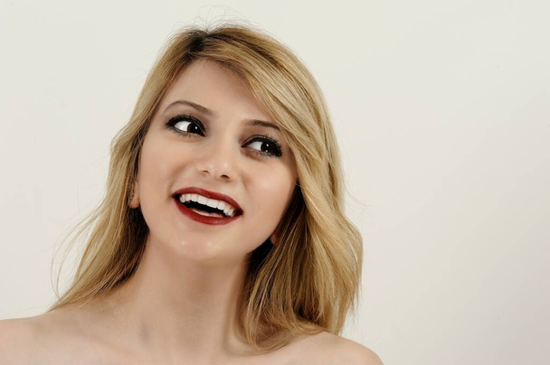 beautiful young woman with blonde and long hair and red lips laughing against a white background - Фото, зображення