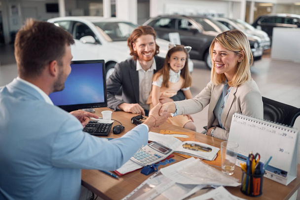Young family in car sales salon buying car and shaking hand with agent  - Foto, imagen