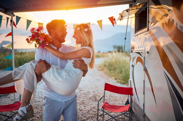 A young man is holding his bride in the arms at the camp on a beautiful day in the nature. Relationship, honeymoon, camping, nature - Foto, Imagen
