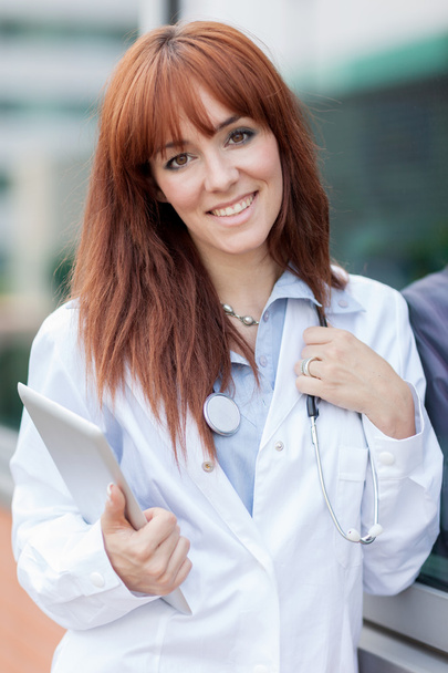 портрет улыбающейся женщины-врача, стоящей снаружи с табличкой р
 - Фото, изображение