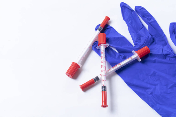 Syringes on top of blue rubber gloves on white background with copy space for text. - Photo, Image