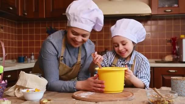 Houden van vrolijke moeder en haar schattige 5 jaar oude dochter in koks hoeden, genieten van samen koken, plezier hebben, deeg kneden en spelen met bloem tijdens het bereiden van taarten voor paasvakantie - Video