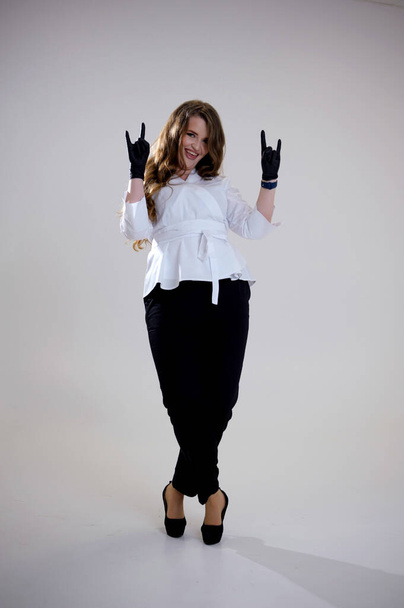 Λεπτός νέος σε λευκή μπλούζα με μεγάλα στήθη και μαύρο denim παντελόνι, τα χέρια σταυρωμένα μπροστά από στέκεται και κοιτάζοντας κάμερα χαμογελώντας, θέτοντας Γυναίκα λευκό oversized πουκάμισο μόδας και μαύρο παντελόνι - Φωτογραφία, εικόνα