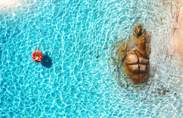 Vista aérea de una joven nadando con un anillo de natación rojo en el mar azul en el día soleado de verano. Paisaje tropical con chica, agua clara, piedras, playa de arena. Vista superior. Vacaciones en Cerdeña, Italia - Foto, imagen