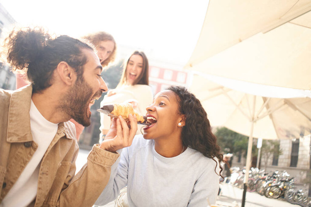 Escena romántica de una pareja compartiendo una comida en su primera cita mientras los amigos miran en el fondo. Foto de alta calidad - Foto, imagen