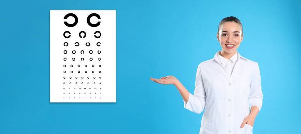 Vision test. Ophthalmologist or optometrist pointing at eye chart on light blue background, banner design - Фото, изображение