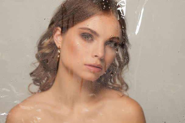 Beautiful young woman posing through transparent film on grey background - Foto, imagen