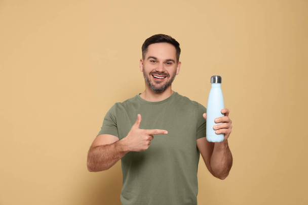 Happy man pointing on thermo bottle against beige background - Zdjęcie, obraz