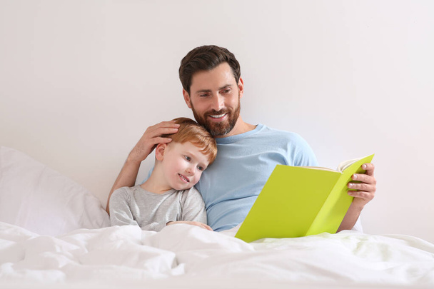 Father reading book with his child on bed at home - Fotoğraf, Görsel