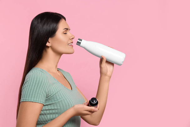 Young woman drinking from thermo bottle on pink background. Space for text - Fotó, kép