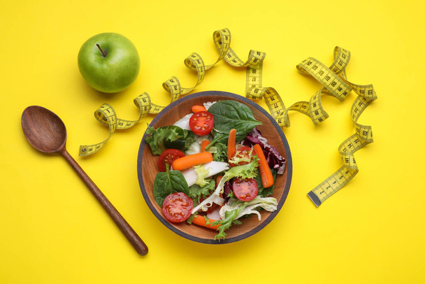 Measuring tape, vegetable salad and apple on yellow background, flat lay. Weight loss concept - Fotó, kép