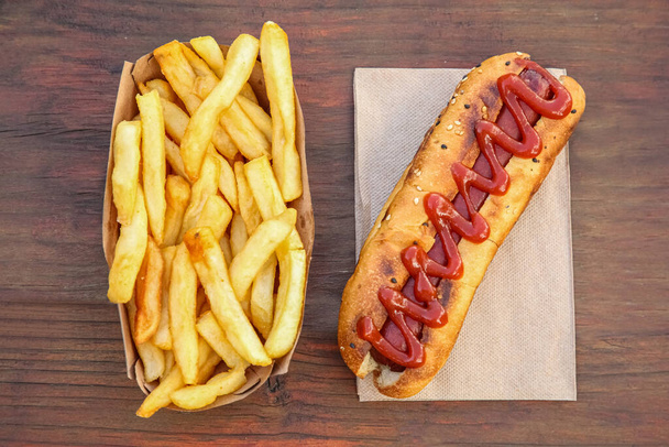 Fresh tasty hot dog and french fries on wooden table, flat lay - Foto, Imagen