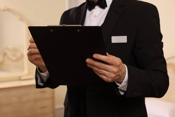 Man in suit with clipboard indoors, closeup. Professional butler courses - Foto, Imagen