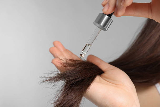 Woman applying essential oil onto hair on light grey background, closeup - Photo, Image