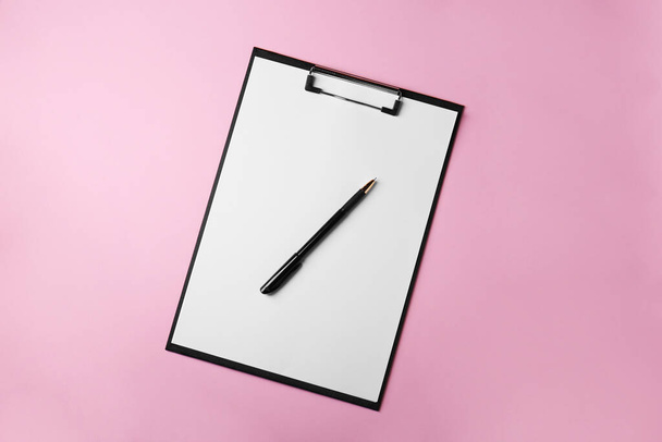 Black clipboard with sheet of blank paper and pen on pink background, top view - 写真・画像