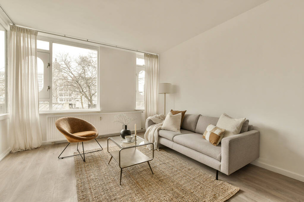 ein Wohnzimmer mit Sofa, Stuhl und Couchtisch vor einem großen Fenster mit Blick auf die Straße - Foto, Bild