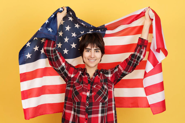 Eine androgyne Person hisst eine US-Flagge im Studio mit gelbem Hintergrund - Foto, Bild