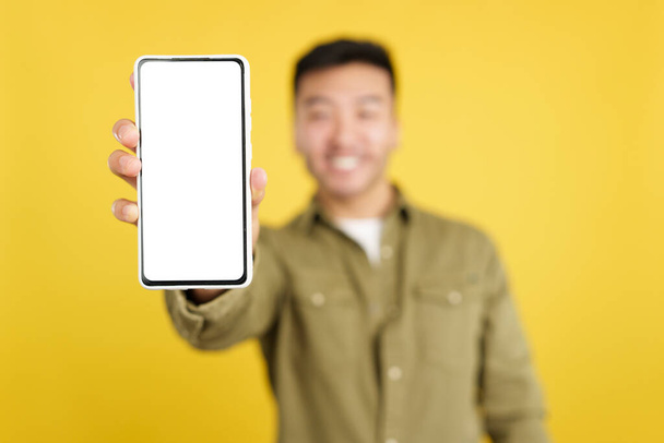 Concéntrese en una pantalla en blanco del móvil en poder de un hombre chino en el estudio con fondo amarillo - Foto, imagen