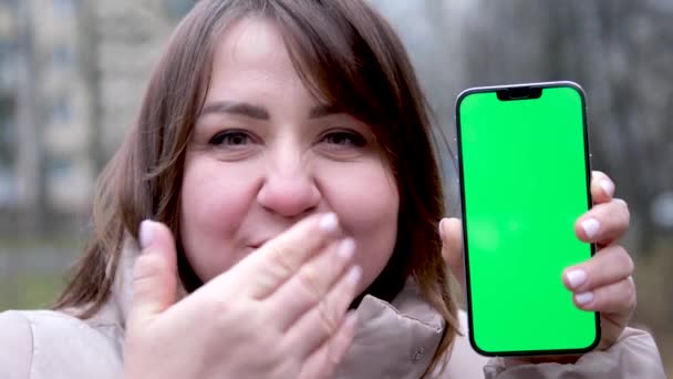 Zralá krásná asijská podnikatelka ukazující telefon. zakřivená žena foukání polibek drží zelenou chroma klíč telefon venku podzim-jaro zima s úsměvem ukazuje Wow Velmi cool radost  - Záběry, video