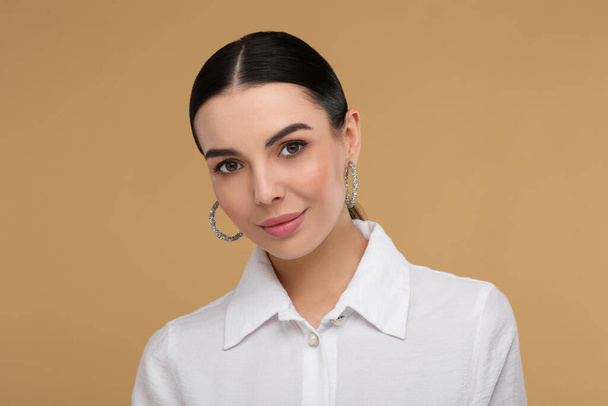 Beautiful young woman with elegant earrings on beige background - Φωτογραφία, εικόνα