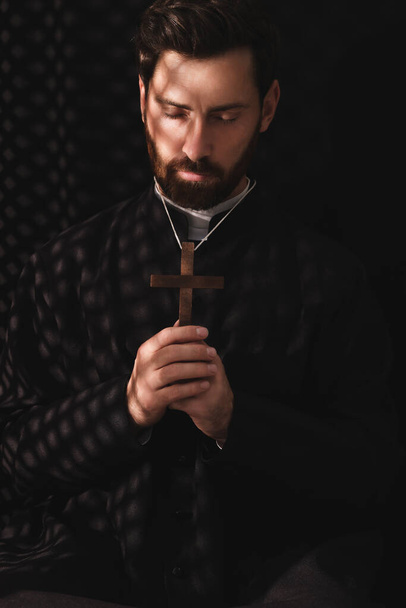 Catholic priest in cassock holding cross and praying to God in confessional - Fotó, kép