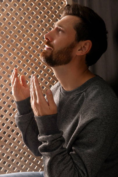 Man praying to God during confession in booth - Фото, изображение