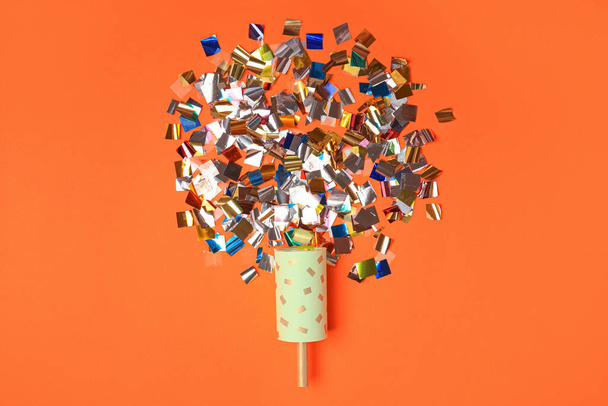 Party popper and colorful confetti on orange background, flat lay - Foto, Imagem