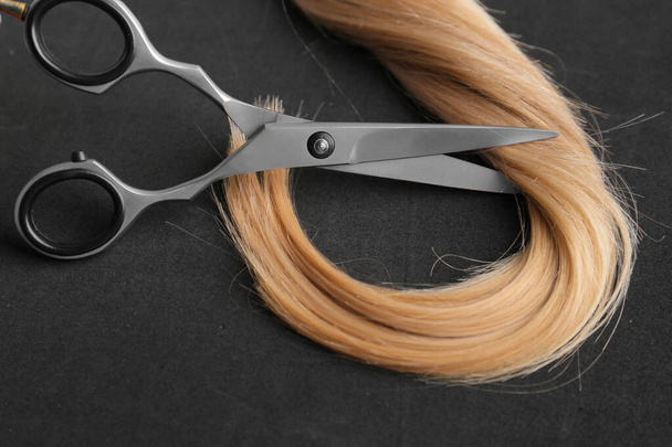 Scissors and piece of blond hair. Professional barber hair cutting shears on background. Hairdresser salon equipment concept, premium hairdressing set. Accessories for haircut with copy space - Foto, imagen
