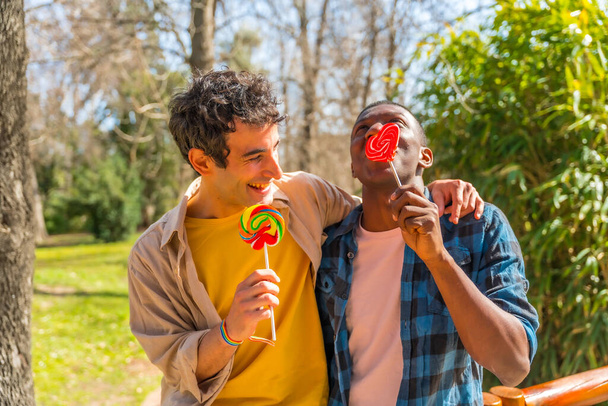 Couple of multi ethnic men eating a lollipop, lgbt concept, having fun and smiling - Фото, зображення