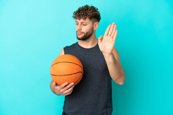Guapo joven jugando baloncesto aislado sobre fondo azul haciendo stop gesture y decepcionado - Foto, imagen