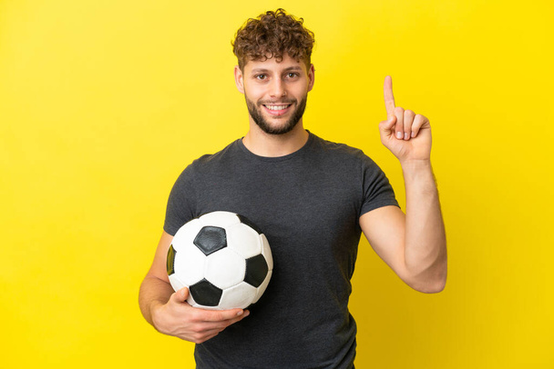 Όμορφος νεαρός ποδοσφαιριστής απομονωμένος σε κίτρινο φόντο δείχνοντας μια μεγάλη ιδέα - Φωτογραφία, εικόνα