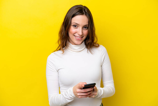 Jonge blanke vrouw geïsoleerd op gele achtergrond het verzenden van een bericht met de mobiele - Foto, afbeelding