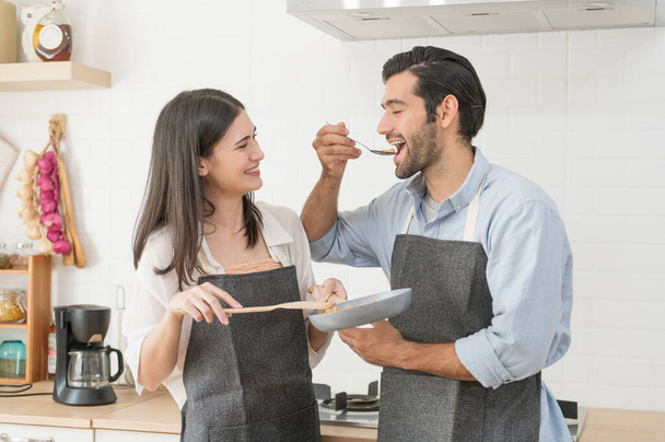 Happy young couple cooking together in the kitchen counter at home - Foto, afbeelding